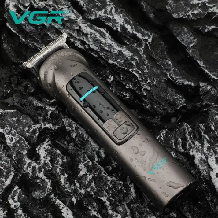A dark gray VGR hair trimmer with a metallic silver blade, shown on a wet, dark textured rock background. The trimmer has a digital display screen and turquoise blue accent lines.